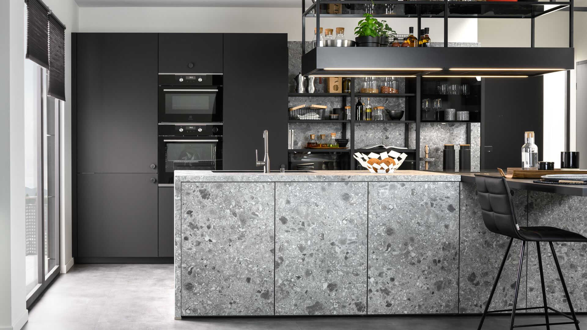 Küche mit Terrazzo Fronten, schwarzen Seitenschränken und hängenden Metallregalen