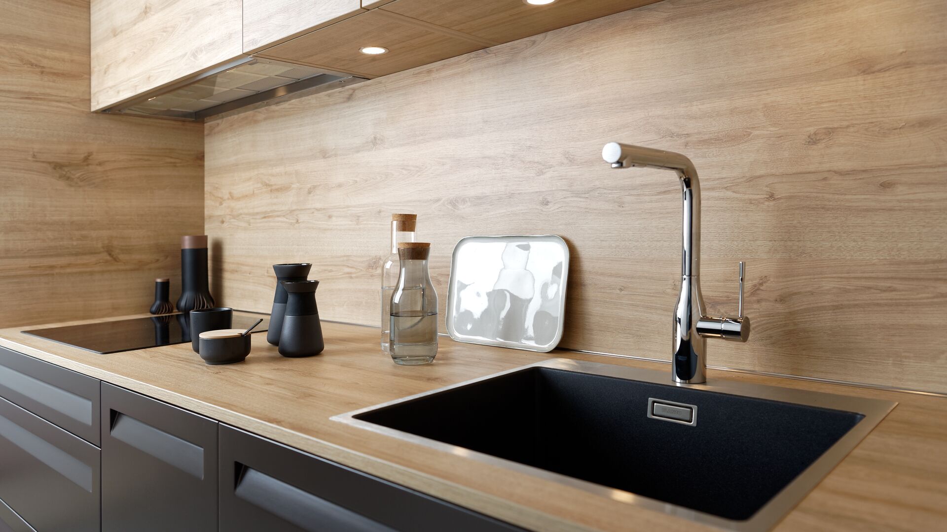 Küche mit Nischenrückwand in Holz, Kochfeld und in Hängeschrank mit Einbauspots integrierter Haube