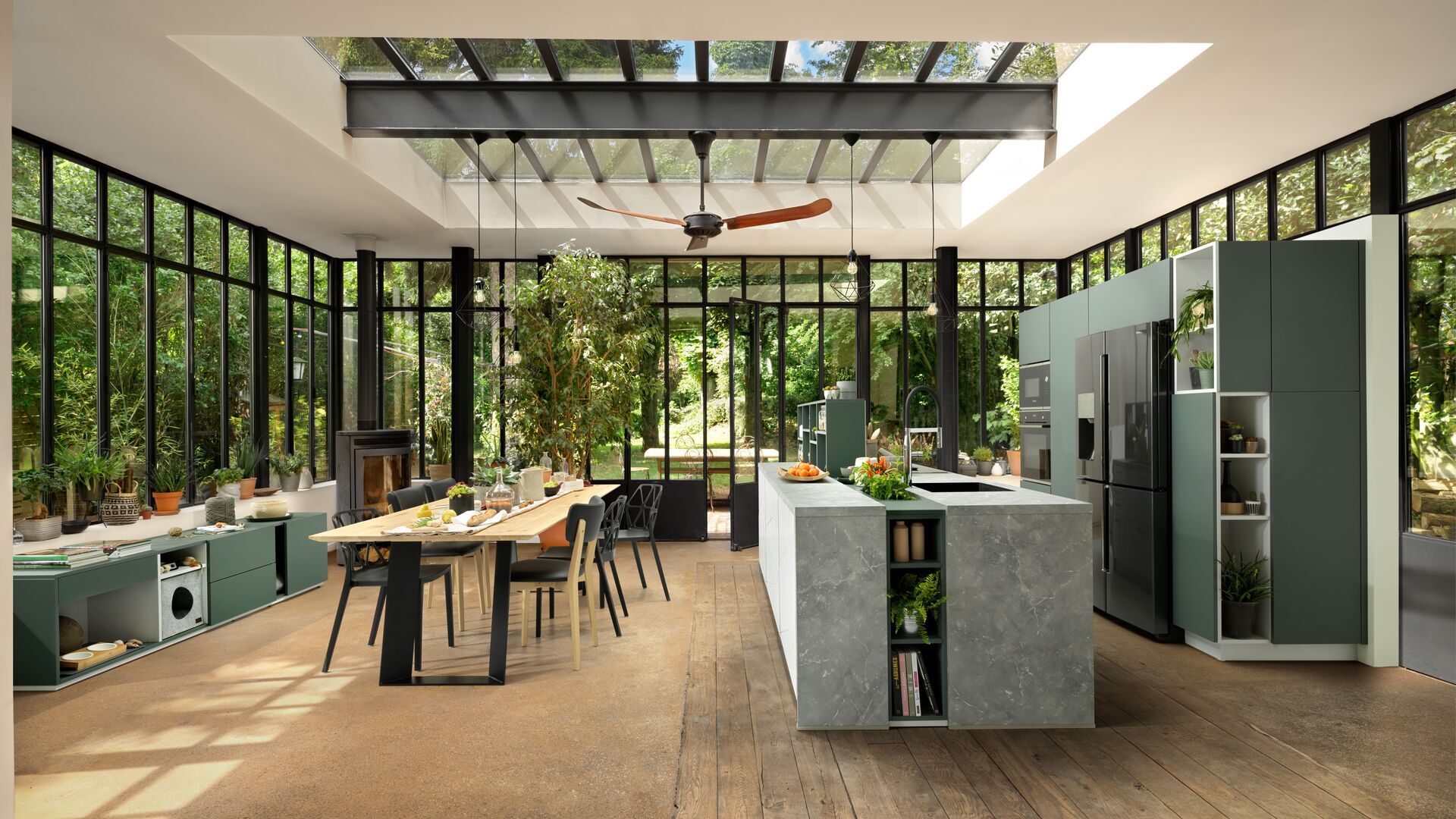 Grijsgroene keuken met eiland en glazen dak met zicht op de tuin in natuurlijke plantensfeer