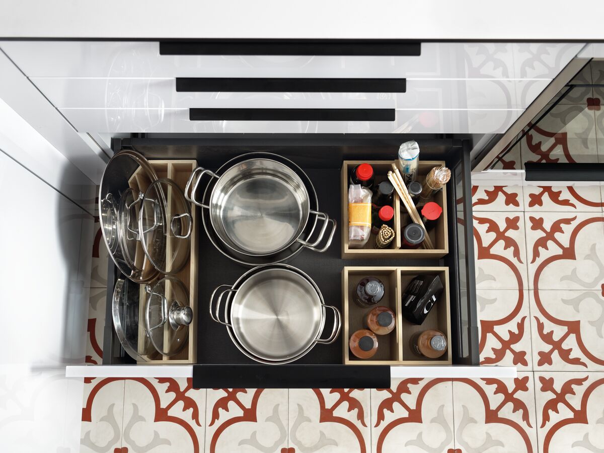 Vue de dessus du meuble bas avec poignées noires et tiroirs blancs dont un ouvert avec des rangements pour casseroles et épices